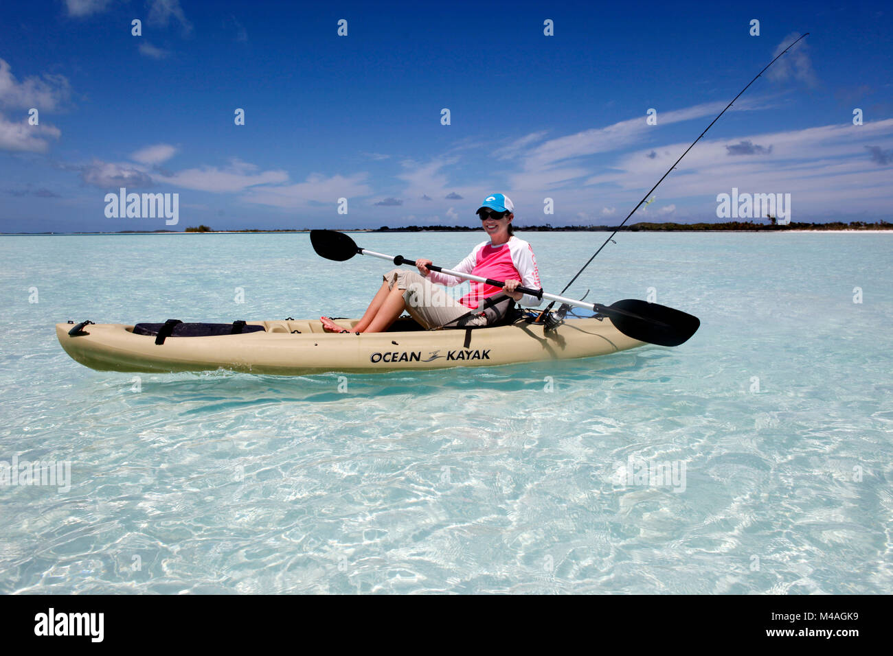 A woman paddles a kayak in the clear Bahamian waters near Man-O-War Cay just off the island of Great Exuma in the Bahamas. Stock Photo