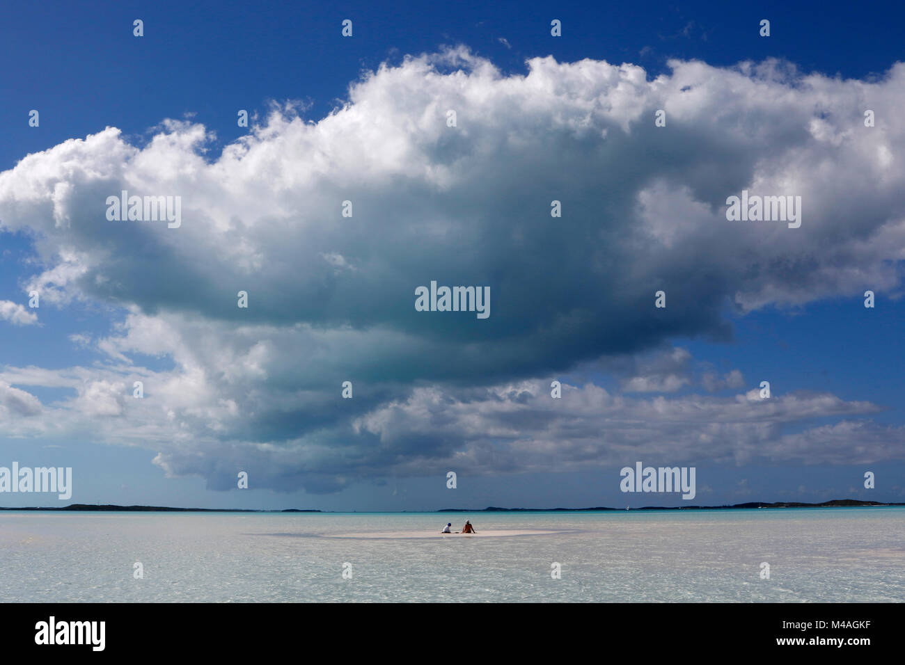 A mother and son sit on a small sand bar in the clear waters near ManO