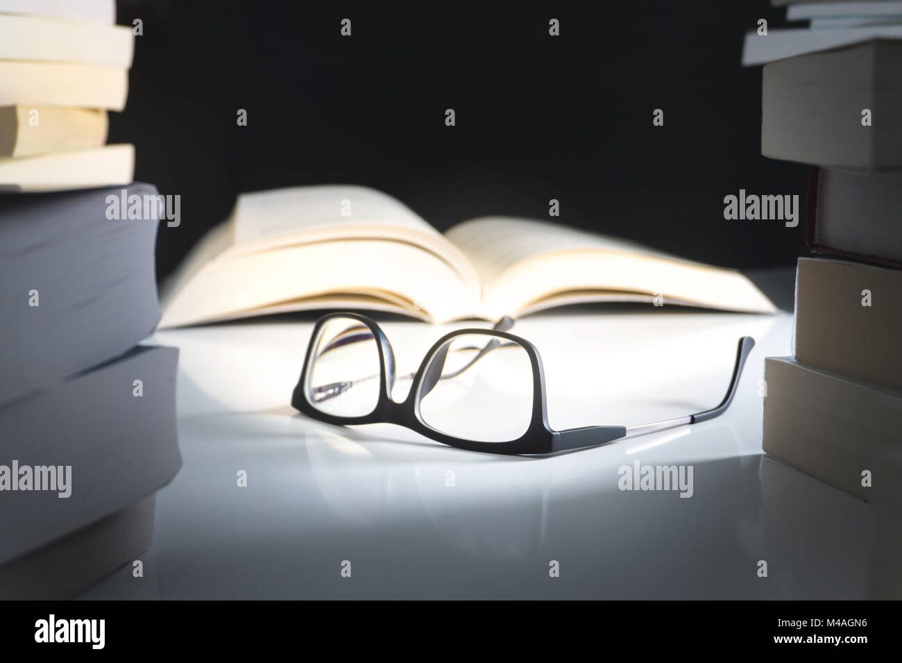 Glasses and open book on table surrounded by literature. Education, learning and reading concept. Stock Photo