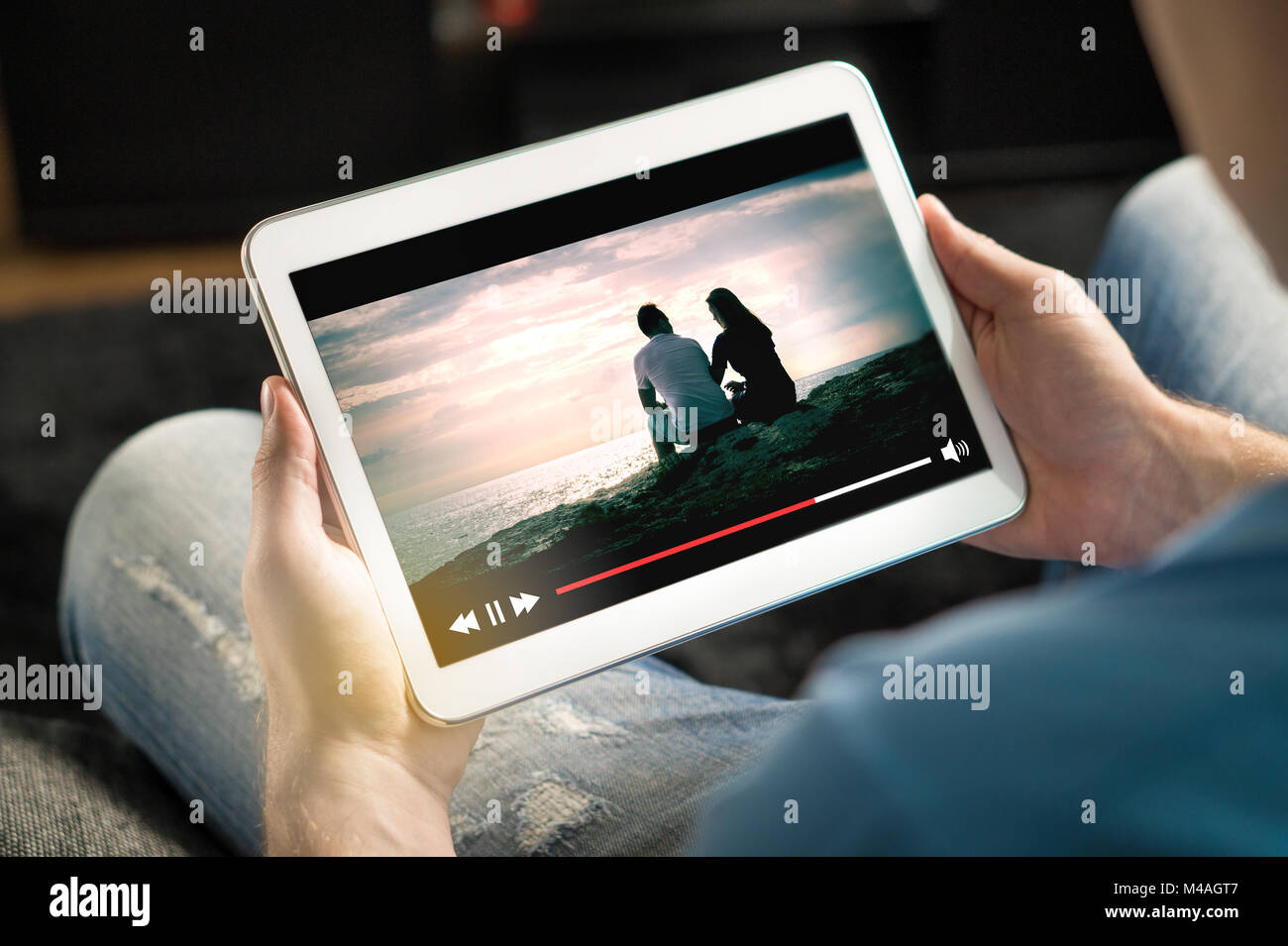 Online movie stream with mobile device. Man watching film on tablet with imaginary video player service. Stock Photo