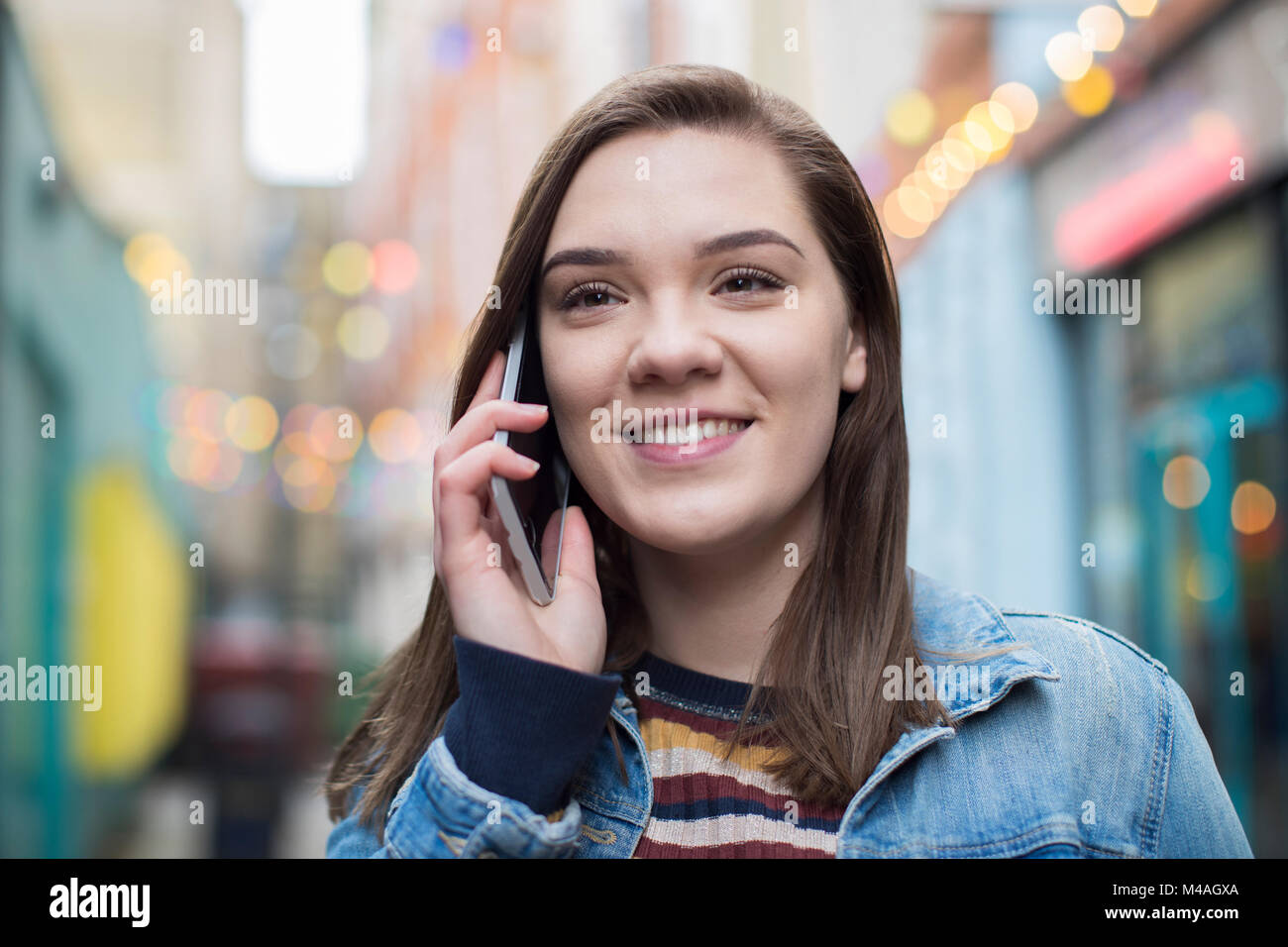 Woman Walking Along City Street Talking On Mobile Phone Stock Photo