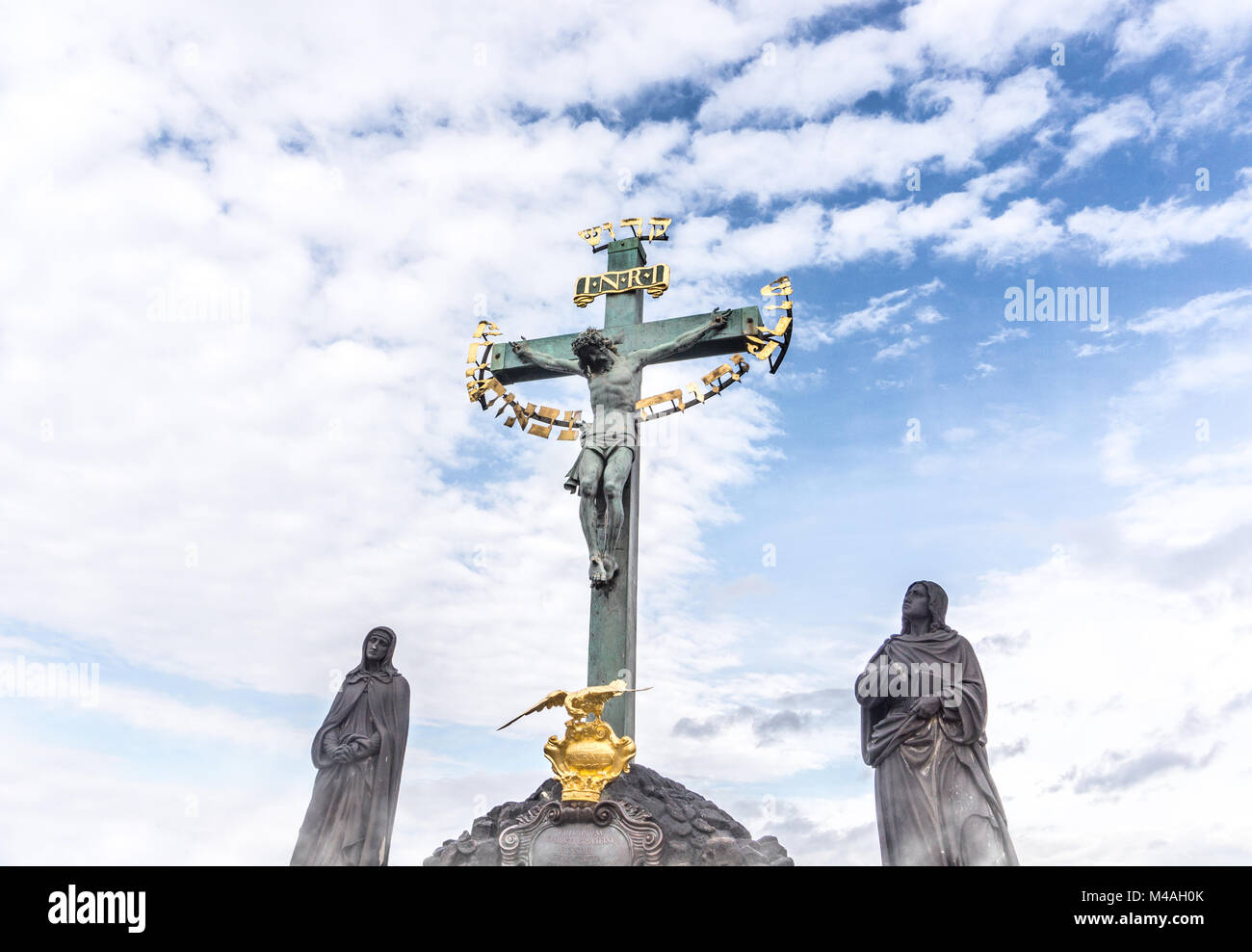Jesus hanging on the cross in a statue. Inri sculpture against blue partly cloudy sky. Stock Photo