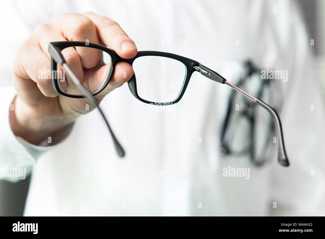 Optician giving new glasses to customer for testing and trying. Eye doctor showing patient lenses. Professional optometrist in white coat. Stock Photo