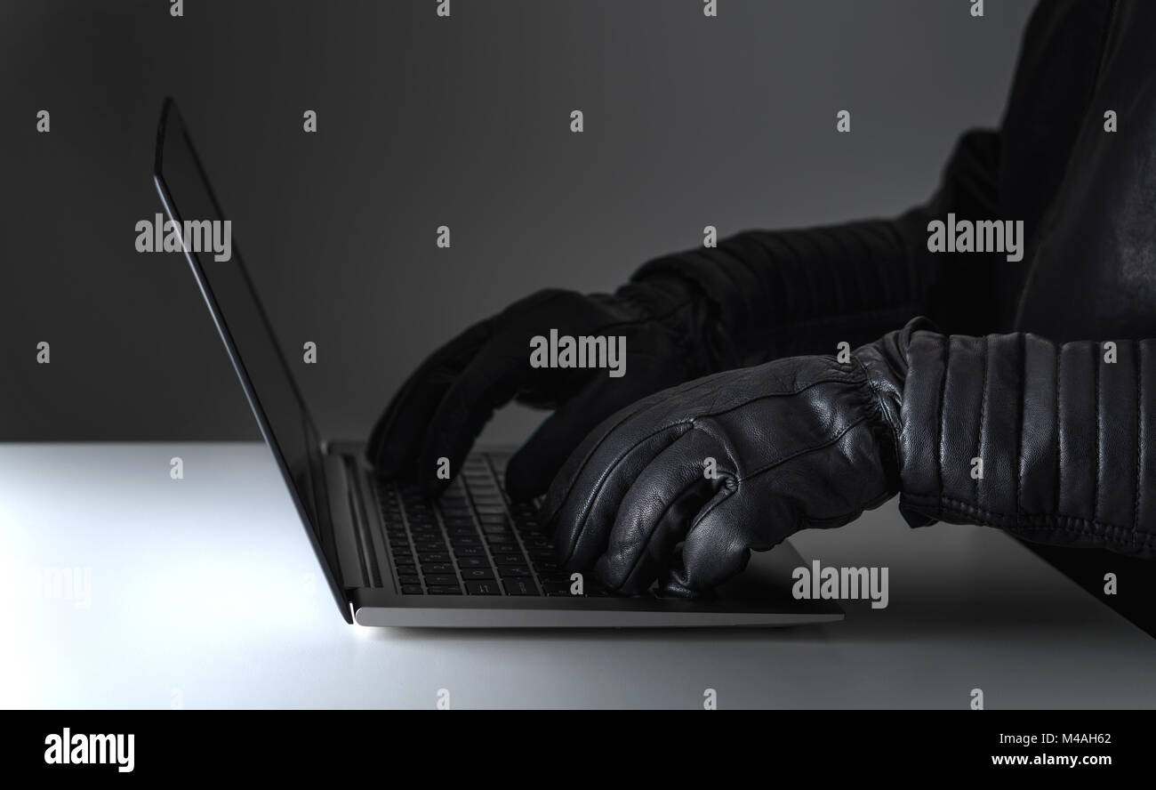 Cyber security threat, attack and online crime concept. Hacker writing with laptop computer wearing leather gloves. Stock Photo