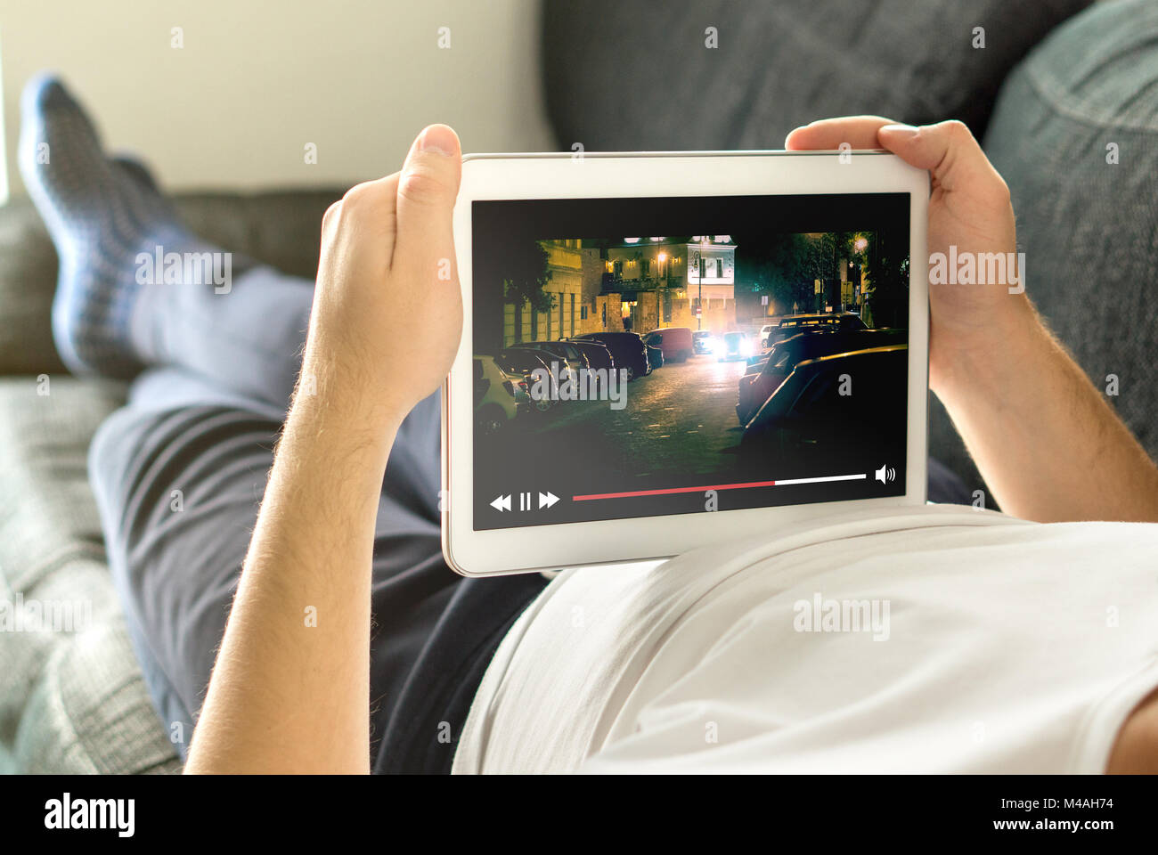 Online movie stream with mobile device. Man watching film on tablet with imaginary video player service. Stock Photo