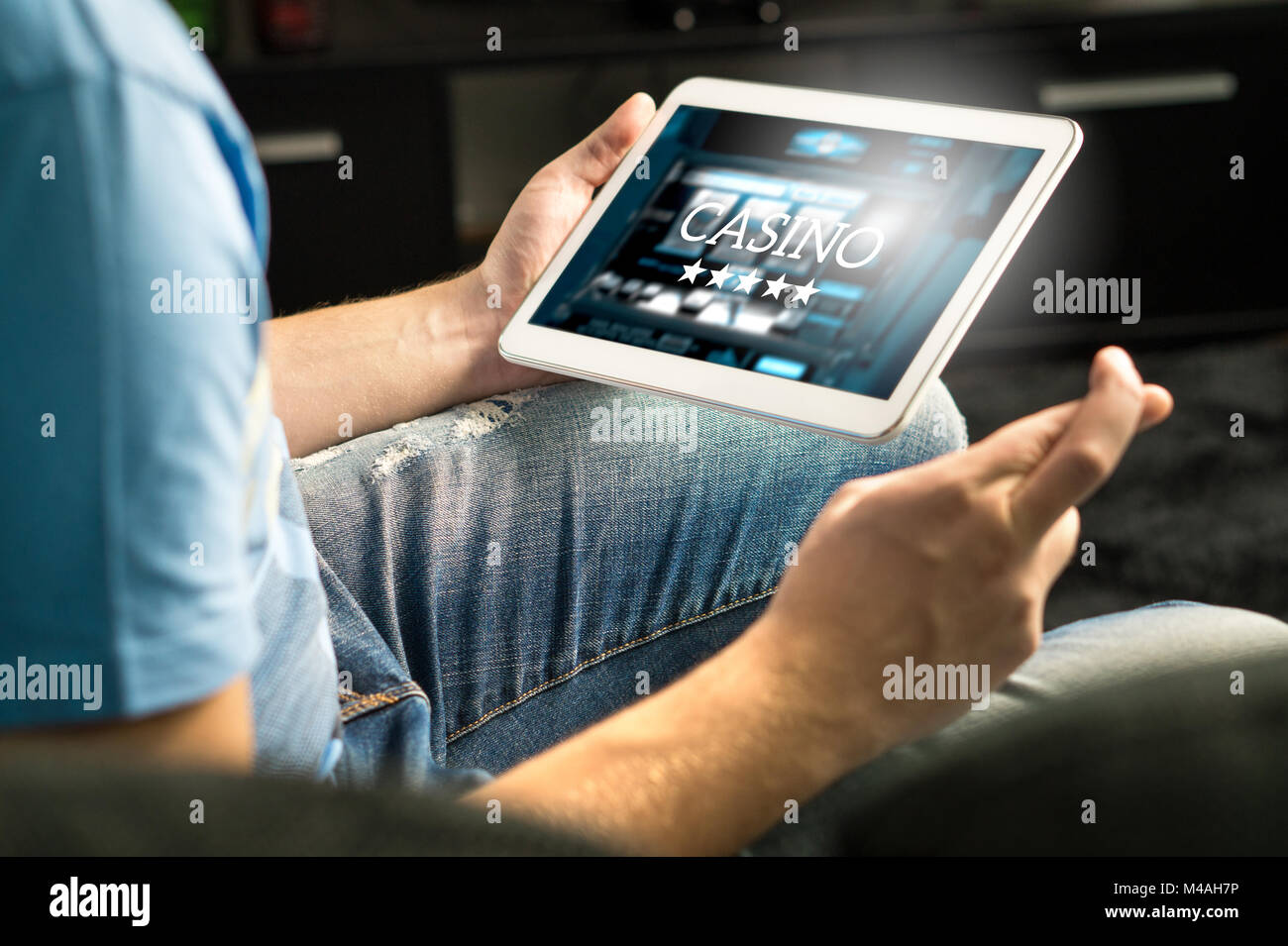 Excited man playing in an online casino with tablet fingers crossed wishing and hoping to win. Slot machine app. Person holding smart mobile device. Stock Photo