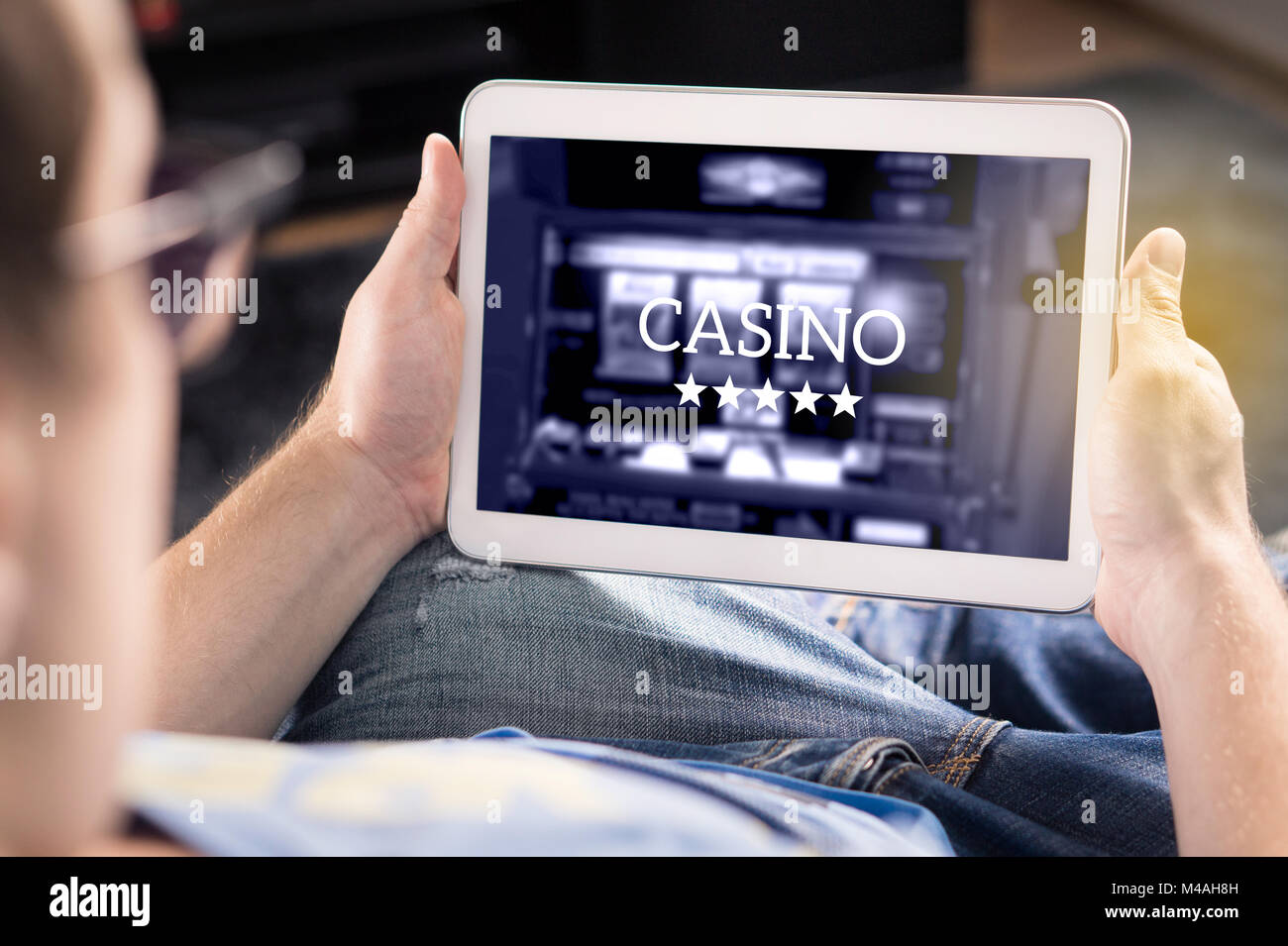 Man playing in an online casino with tablet. Modern gambling application. Slot machine app. Person holding smart mobile device in hand at home. Stock Photo