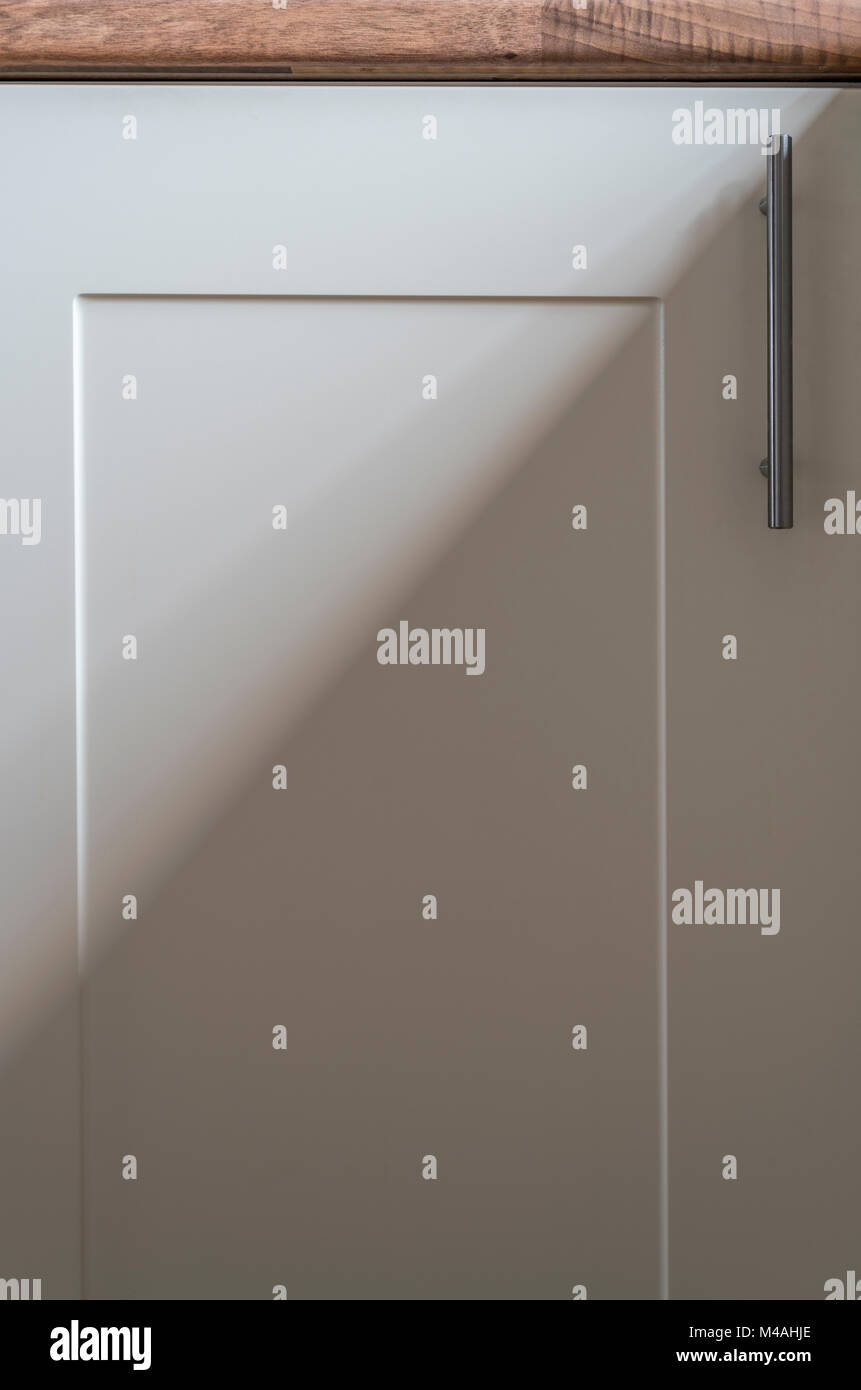 Part of a cream kitchen cabinet door, with stainless handle, a soft shadow cast from an adjacent window. Stock Photo