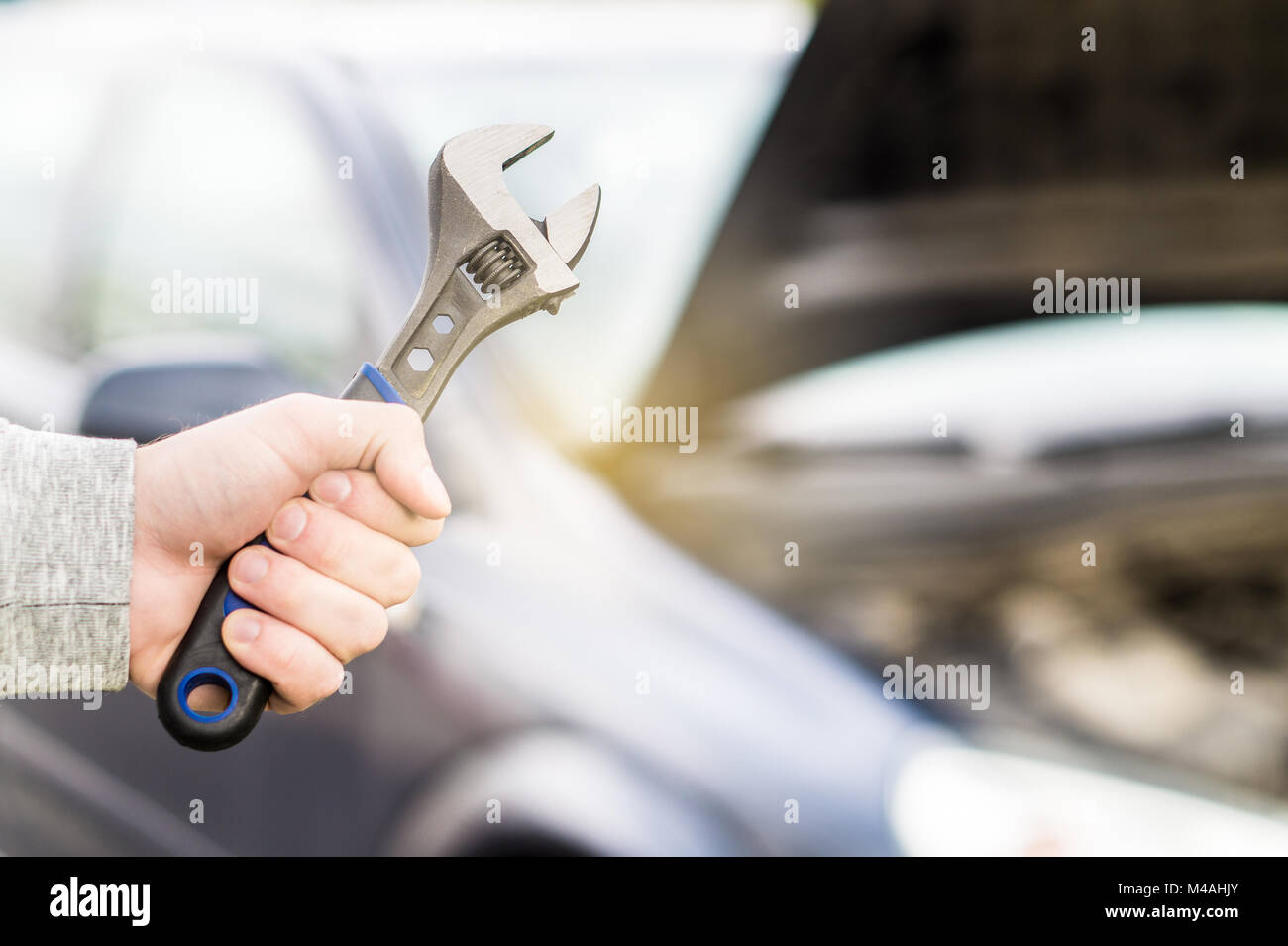 Car repair, maintenance and vehicle inspection concept. Man holding wrench in front of a car with under the hood and engine view. Stock Photo