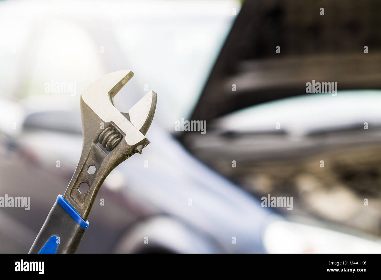 Car repair, maintenance and vehicle inspection concept. Wrench and a car with under the hood and engine view. Selective focus to fixing tool. Stock Photo