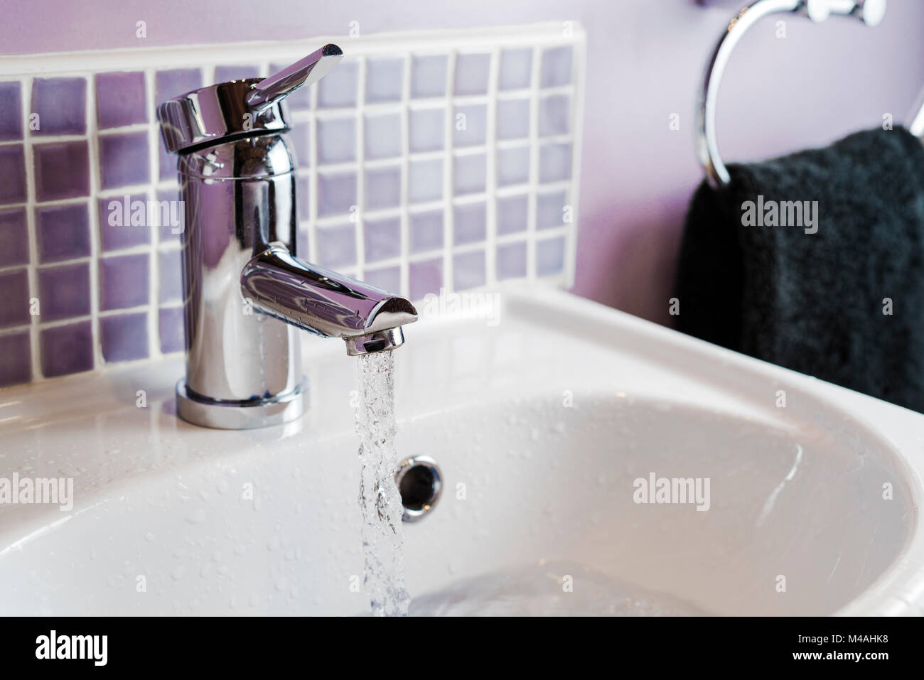 Water running from a bathroom tap or faucet, into a a hand basin. Stock Photo