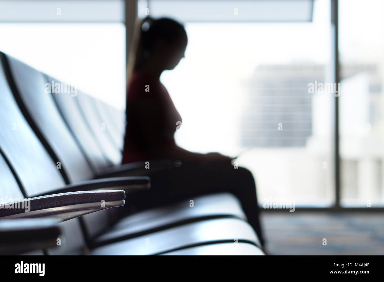 Silhouette woman in airport waiting room. Person sitting on bench before flight in terminal and departure lounge. Travel, holiday and transportation. Stock Photo