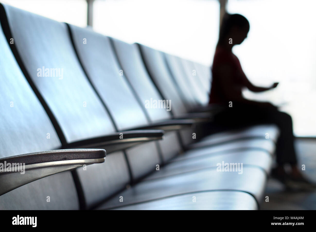 Delayed and cancelled flight concept. Silhouette woman looking her watch in airport terminal to see the time in airport waiting room. Stock Photo
