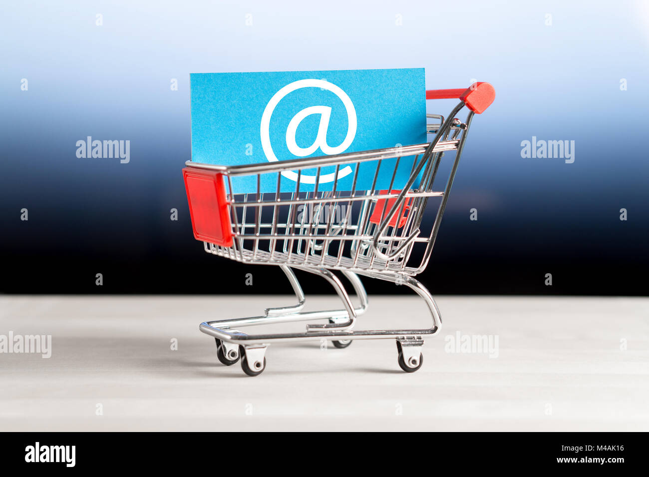 Online shopping, e commerce and internet store concept. Newsletter and email marketing. Miniature shopping cart with at sign. Stock Photo