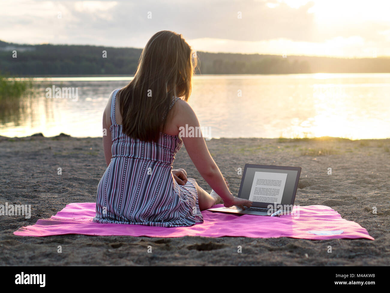 Young attractive woman using laptop on beach at sunset. Active lifestyle. Student doing homework or entrepreneur working late. Stock Photo