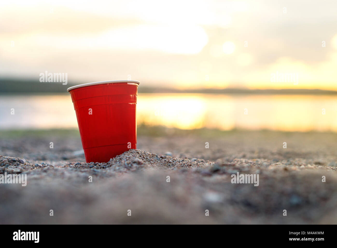 Red party cup in sand at sunset. Summer beach party concept with copy space. Stock Photo