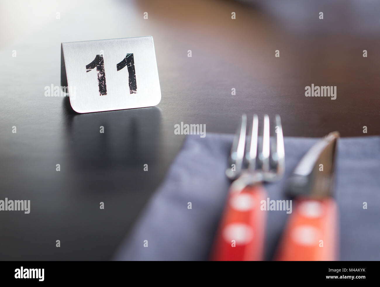 Number sign on restaurant table to show reservation. Utensils, fork and knife in the front. Customer waiting for service or food. Stock Photo