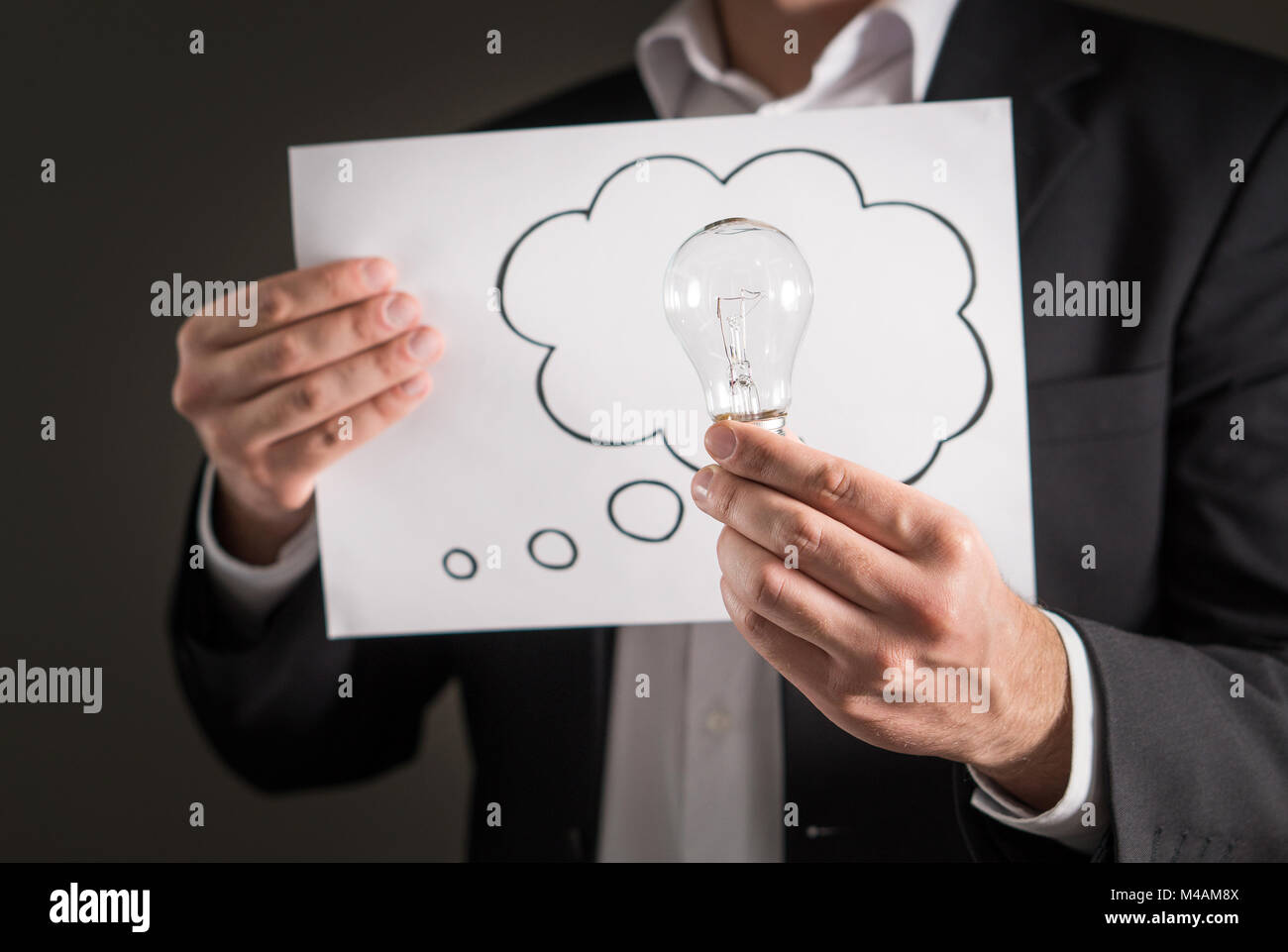 New idea, innovation and brainstorming concept. Business man in a suit holding light bulb and a paper with thinking speech bubble balloon and thought  Stock Photo