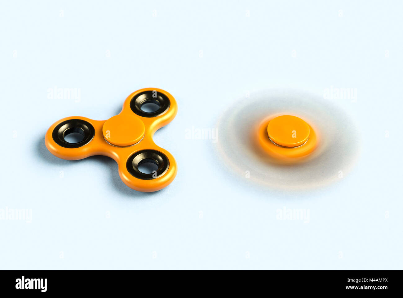 Two fidget spinners on light background, table and platform. One standing still and stopped and the other spinning fast with motion blur. Stock Photo