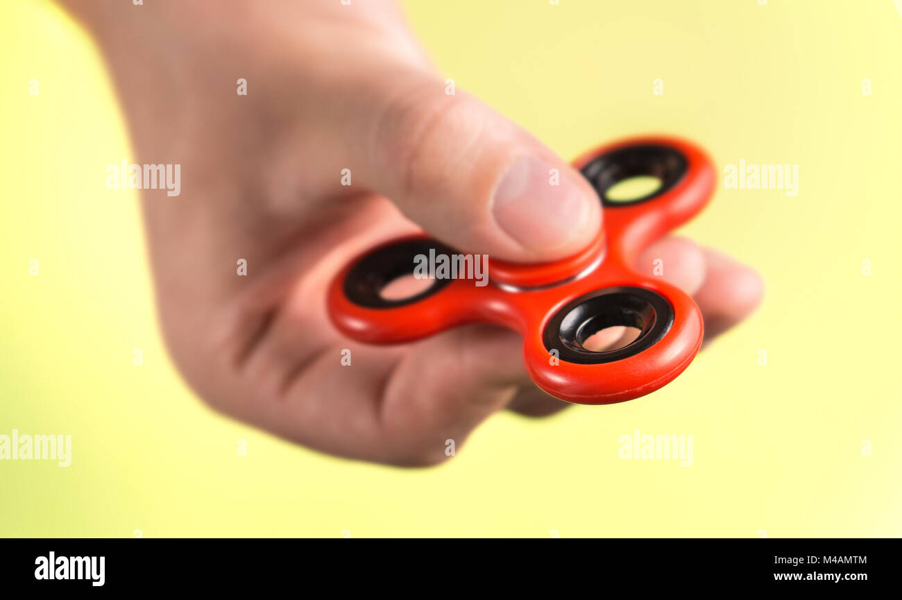 Red fidget spinner between fingers against light yellow background. Stock Photo
