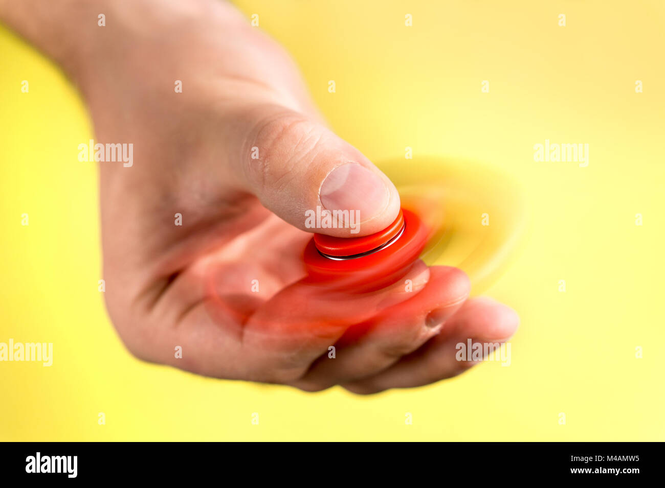 Red fidget spinner spinning fast between fingers against light yellow background. Stock Photo