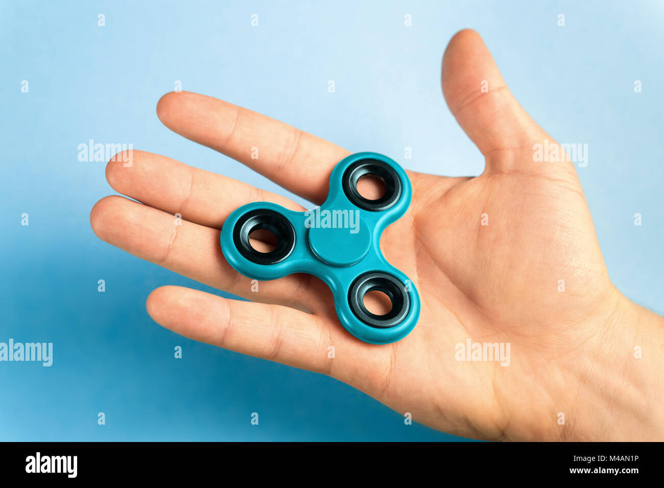 Hand holding fidget spinner with blue background. Stock Photo