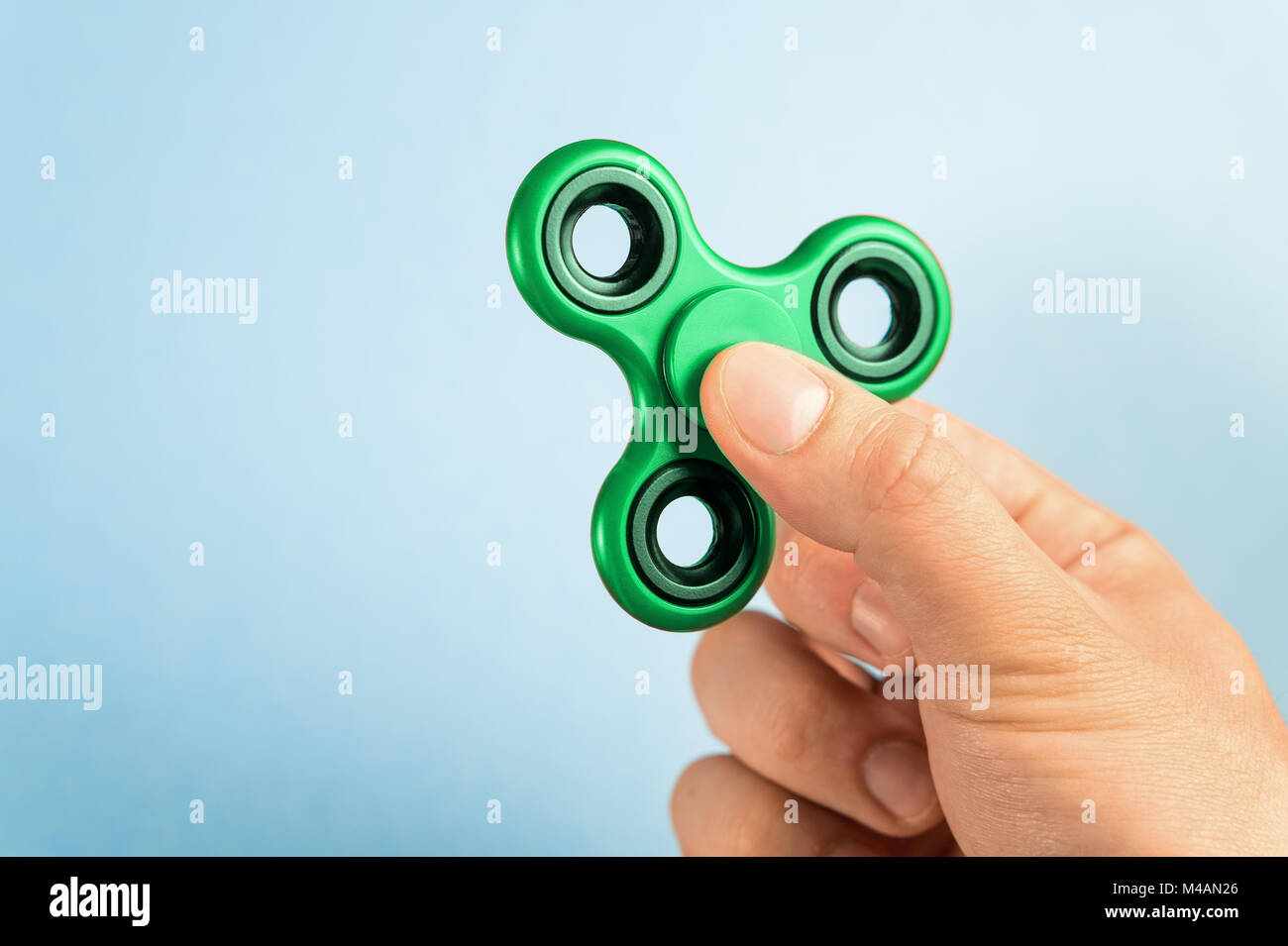 Fidget spinner between fingers against blue background. Stock Photo