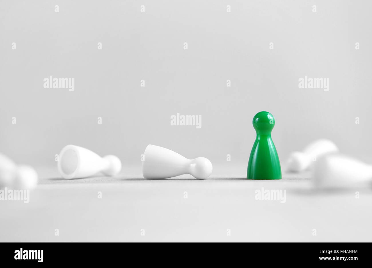 Winning, victory, success and surviving concept. Green board game pawn stand alone, the white rest fallen. Eliminating competitors. Stock Photo