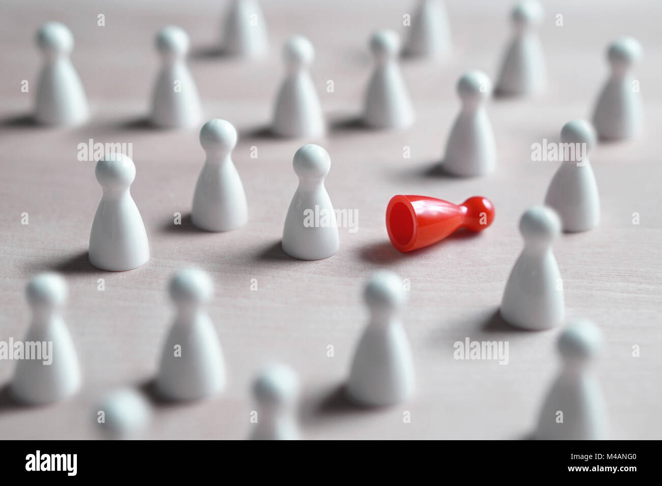 Racism, bullying, social exclusion, depression and loneliness concept. A lot of white board game pawns, one red fallen on its side. Stock Photo
