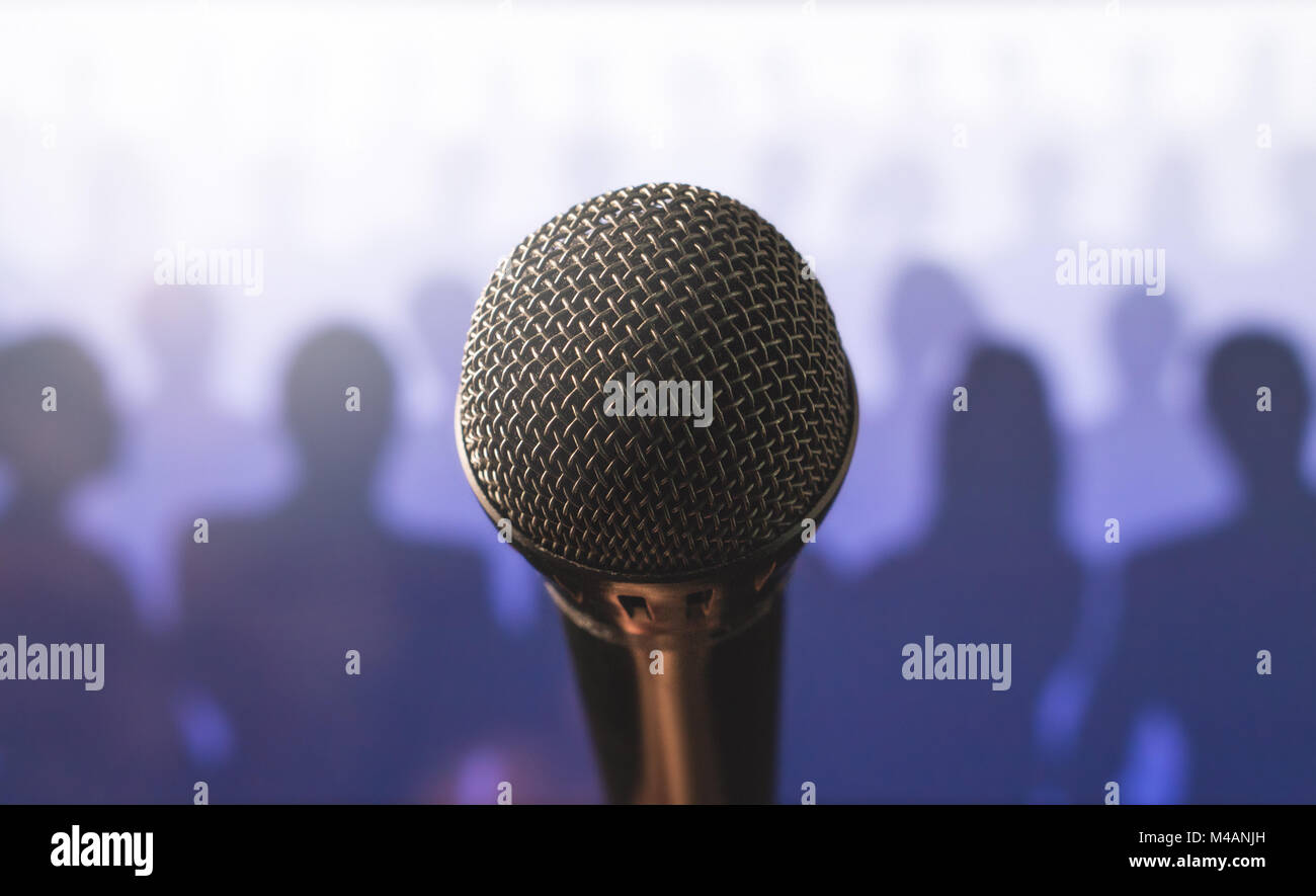 Close up of microphone in front of a silhouette audience and crowd of people. Public speaking and giving speech. Stage fright or training to talk. Stock Photo