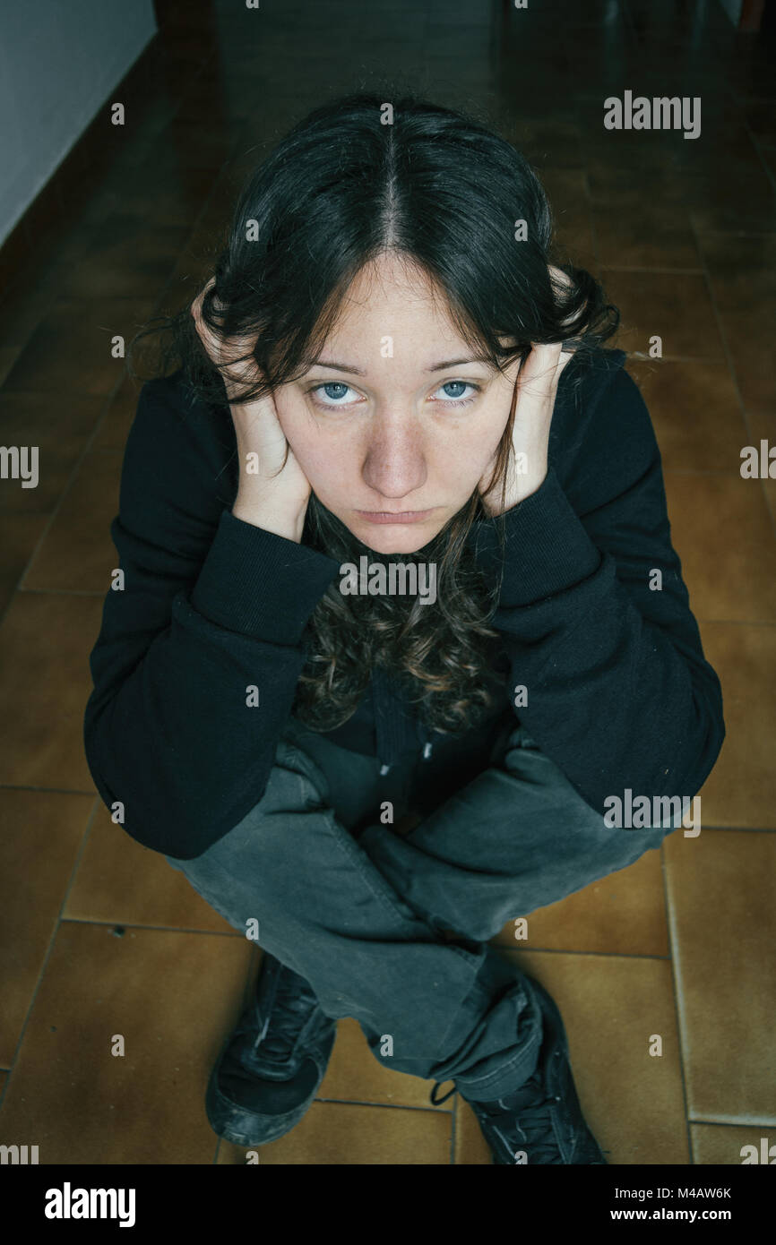 thoughtful girl with long hair sitting on the floor with her hands on ...