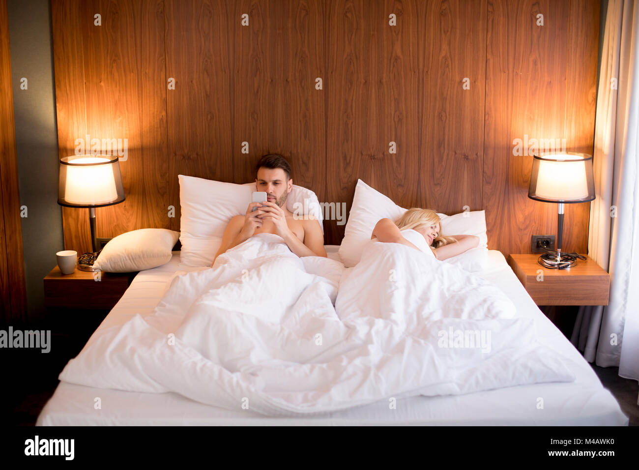 Young man looking at phone while woman sleeping in the room Stock Photo