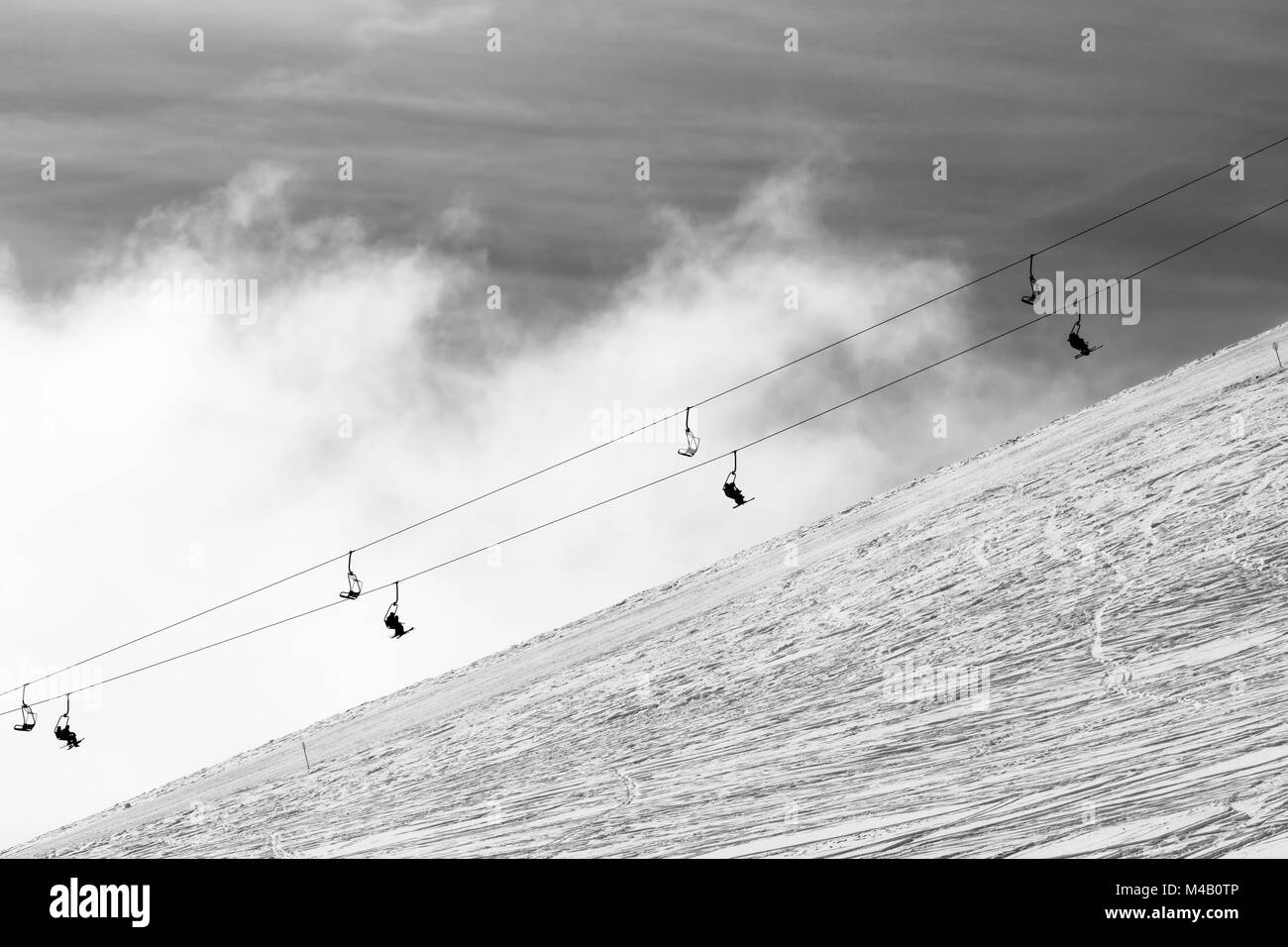 Snowy off-piste ski slope and silhouette of chair-lift in fog. Caucasus ...