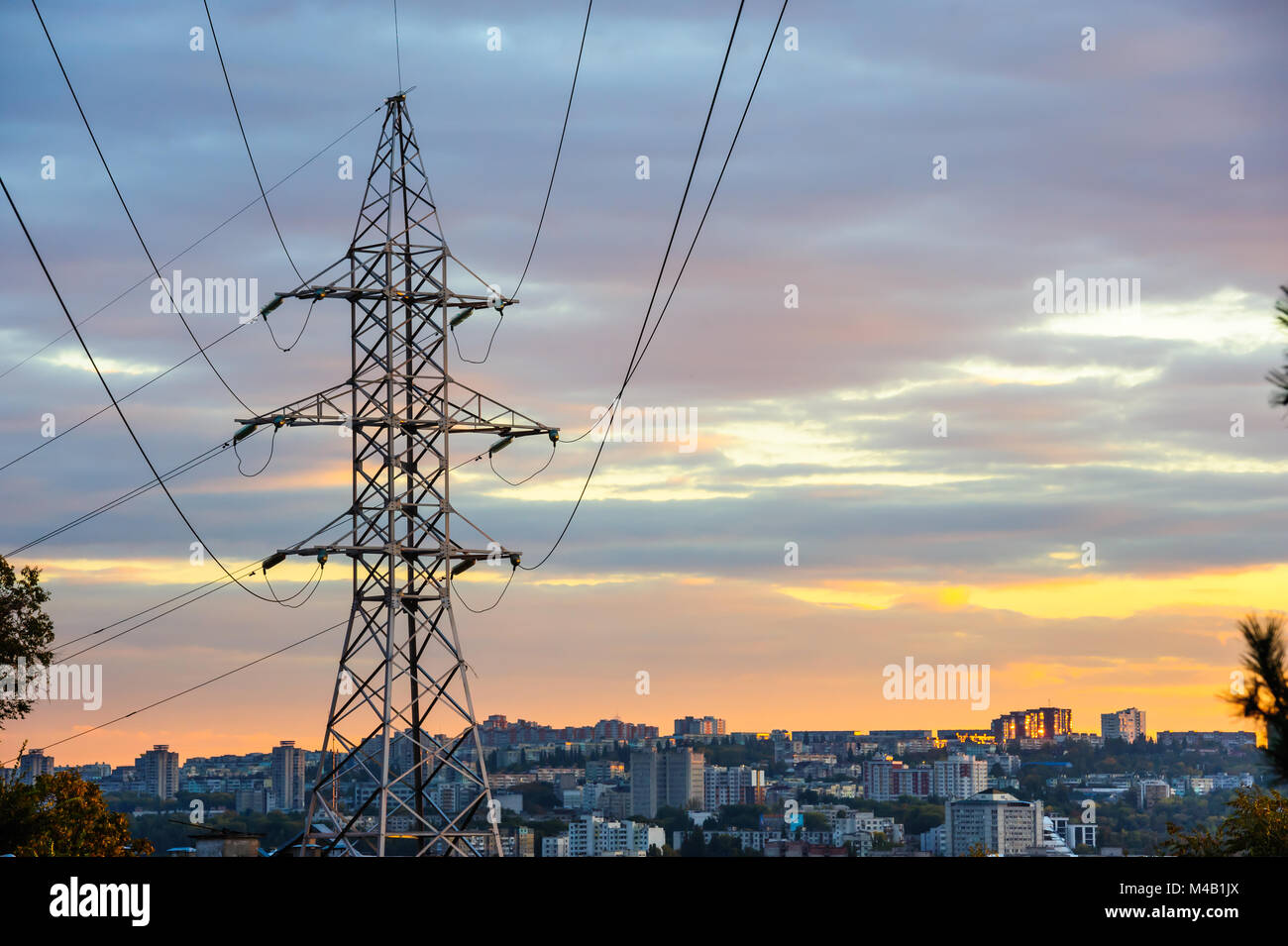 Electricity pylons and power lines silhouettes at a cloudy sunset. Stock Photo