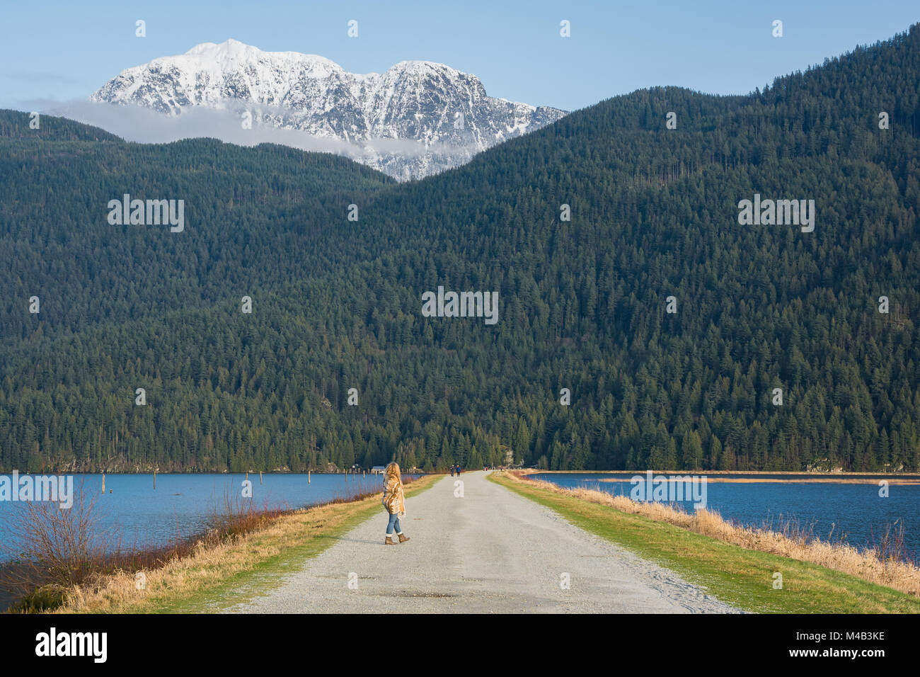 A girl on a walking trail surrounded by snow capped mountains Stock Photo