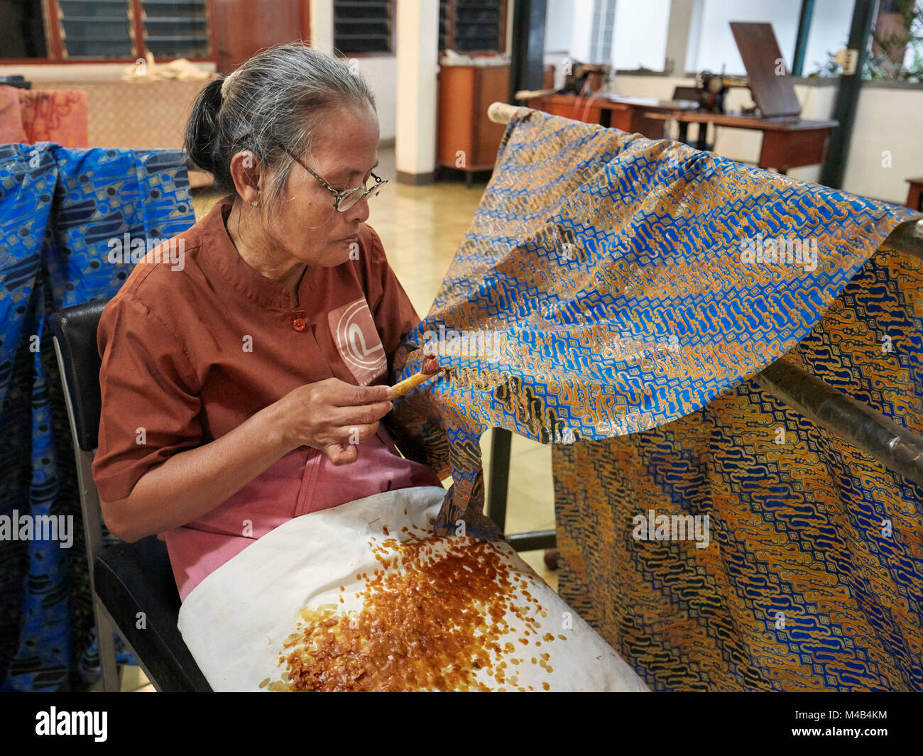 Craftswoman applying hot wax-resist dyeing on batik with a canting (spouted tool). Batik Winotosastro shop, Yogyakarta, Java, Indonesia. Stock Photo
