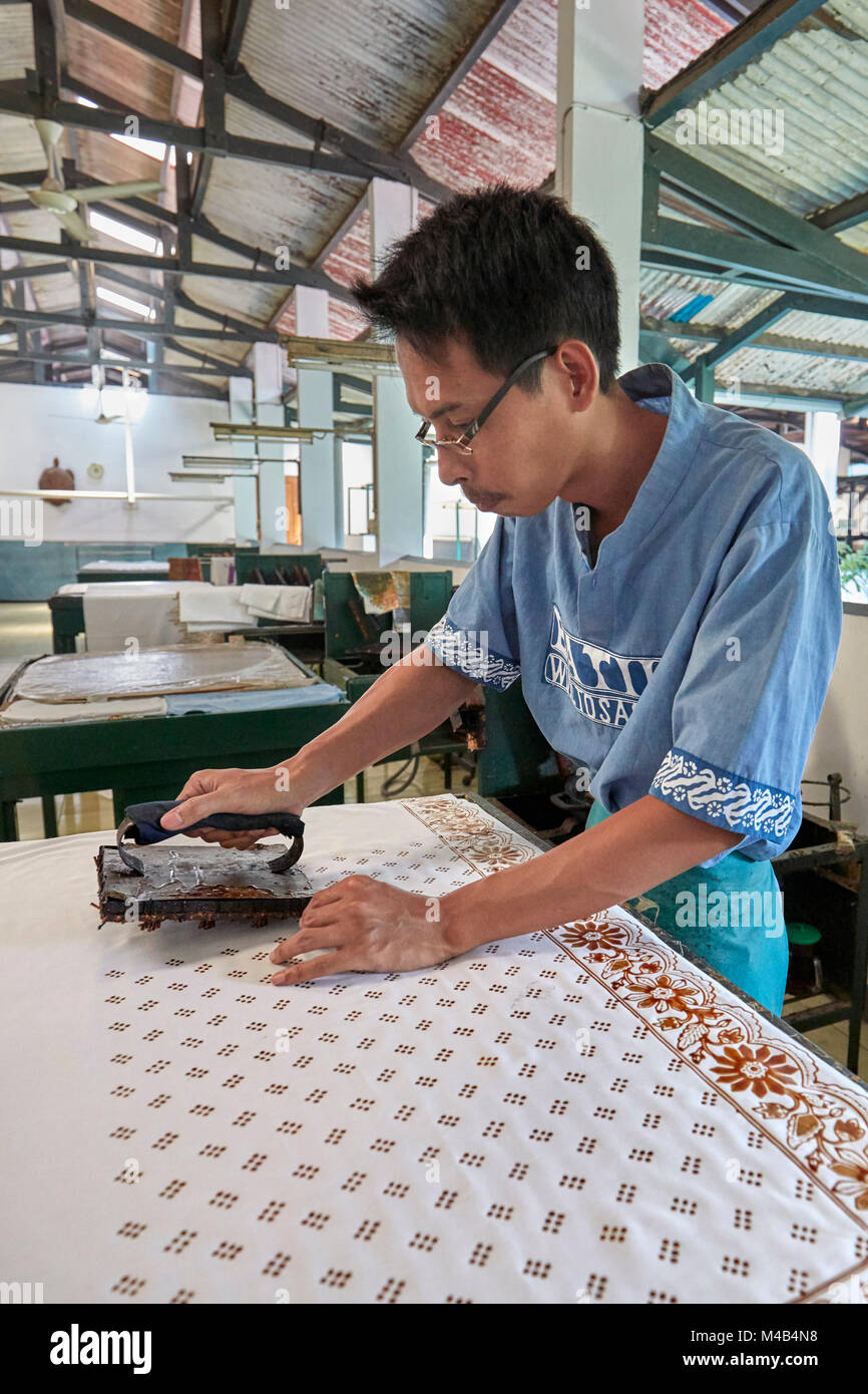 Batik maker printing the hot wax-resist dyeing on a cloth with a Cap (copper stamp). Batik Winotosastro shop, Yogyakarta, Java, Indonesia. Stock Photo