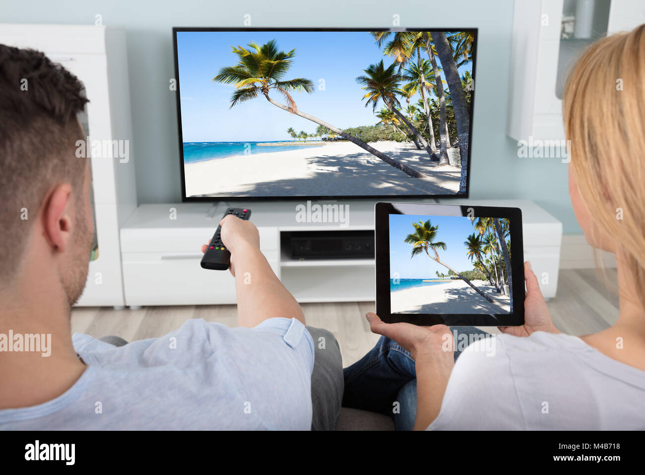 Rear View Of Couple Connecting Television Channel Through WiFi On Digital Tablet At Home Stock Photo