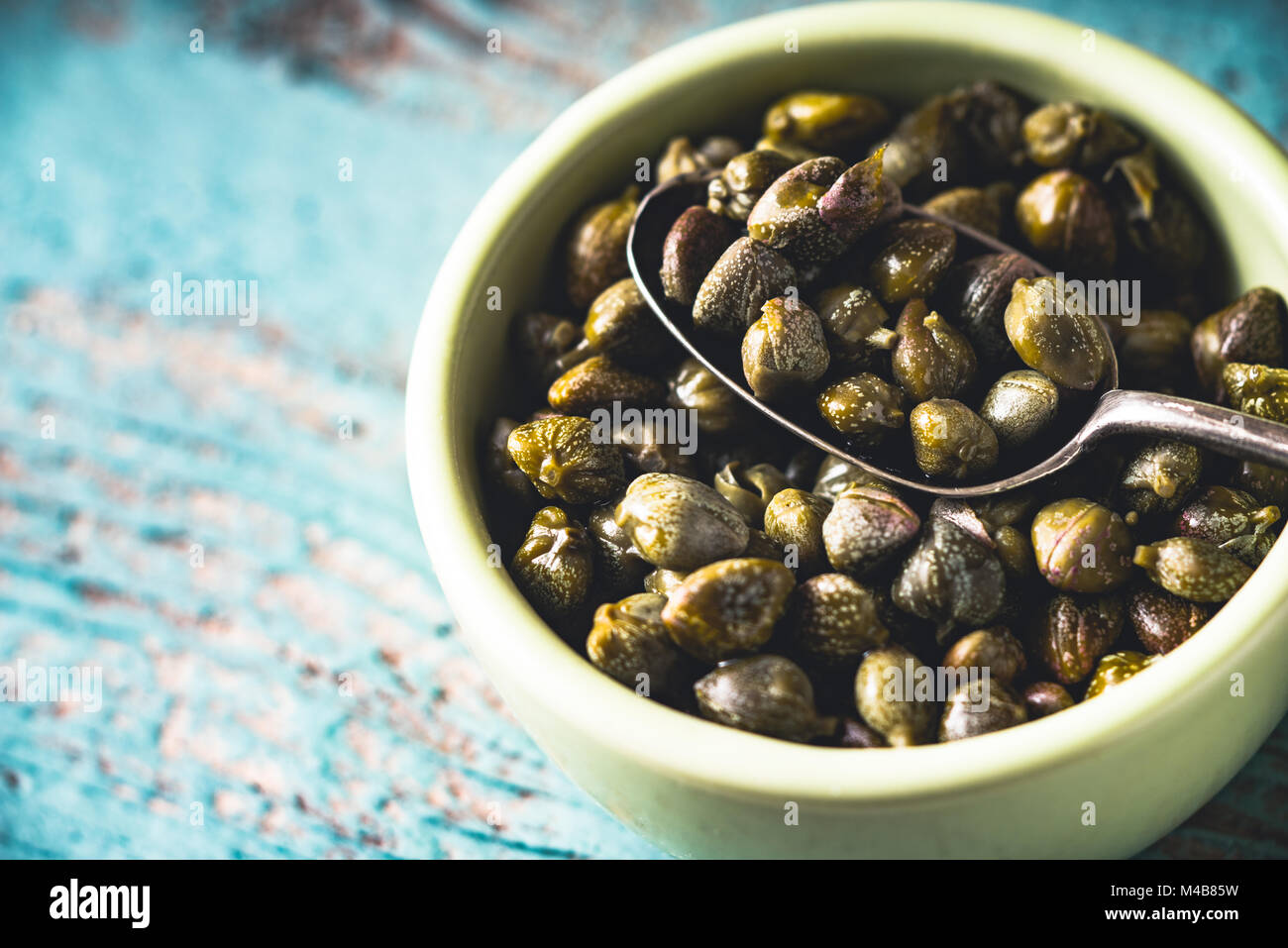 Capers in the bowl on the light blue background Stock Photo