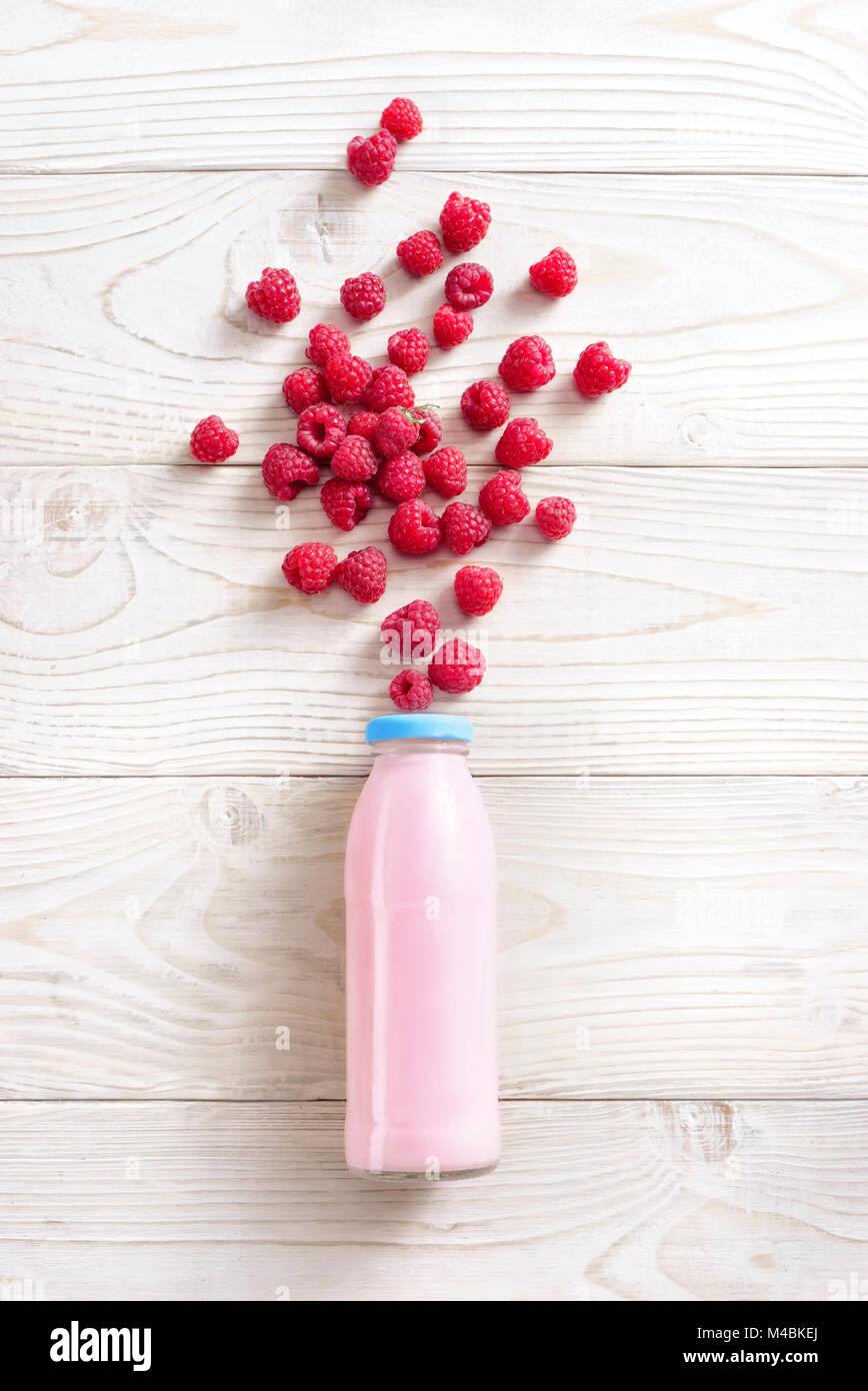 Bottle of yogurt with an explosion of raspberry on wooden table. Fresh