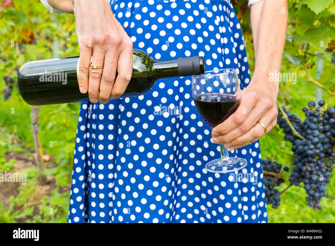 Woman in dress pouring red wine bottle in glass Stock Photo