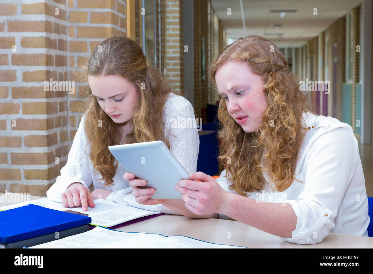 Two teenage girls studying in corridor of school Stock Photo