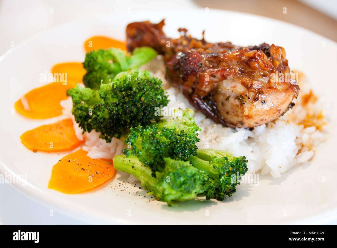 Authentic food prep, juicy roasted chicken drumsticks, homemade, with soy sauce, rice wine, sugar, garlic, oregano; rice with carrot and broccoli Stock Photo