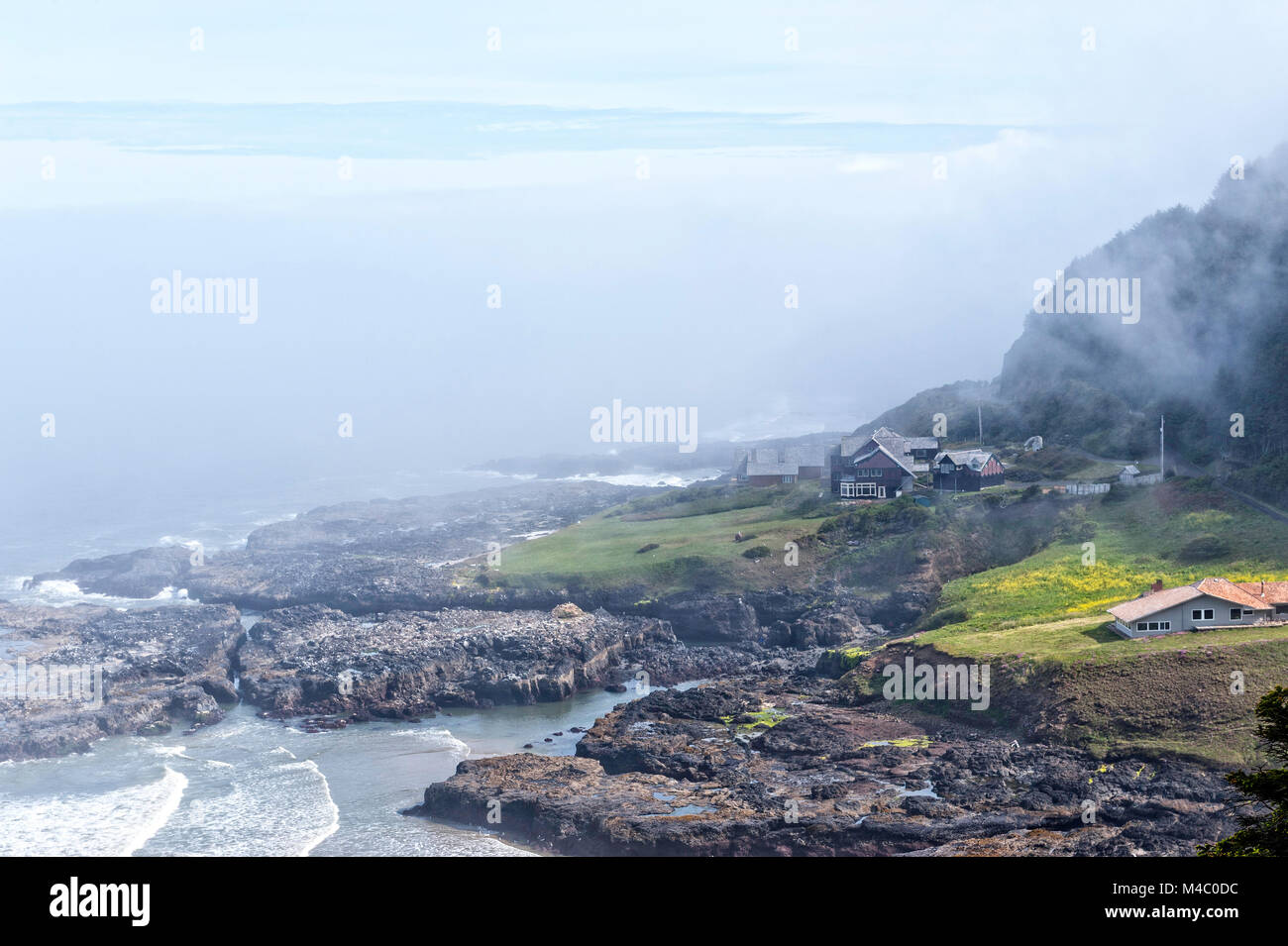 A house sits on the rocky shore of the coast of Oregon in the mist Stock Photo