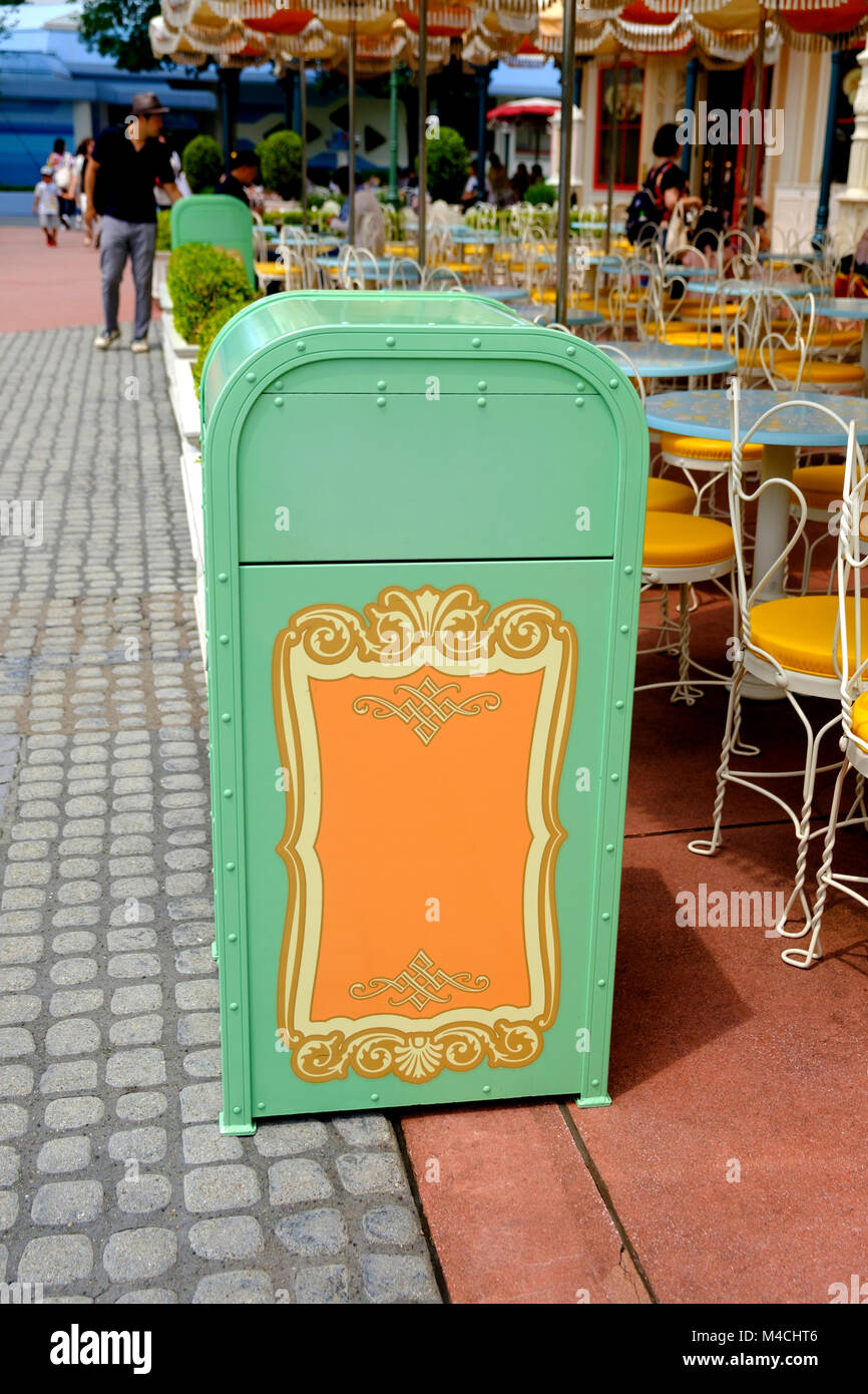 Decorative, beautiful & clean pale green & orange trash bin next to empty round tables outside. -Disneyland Tokyo. Stock Photo