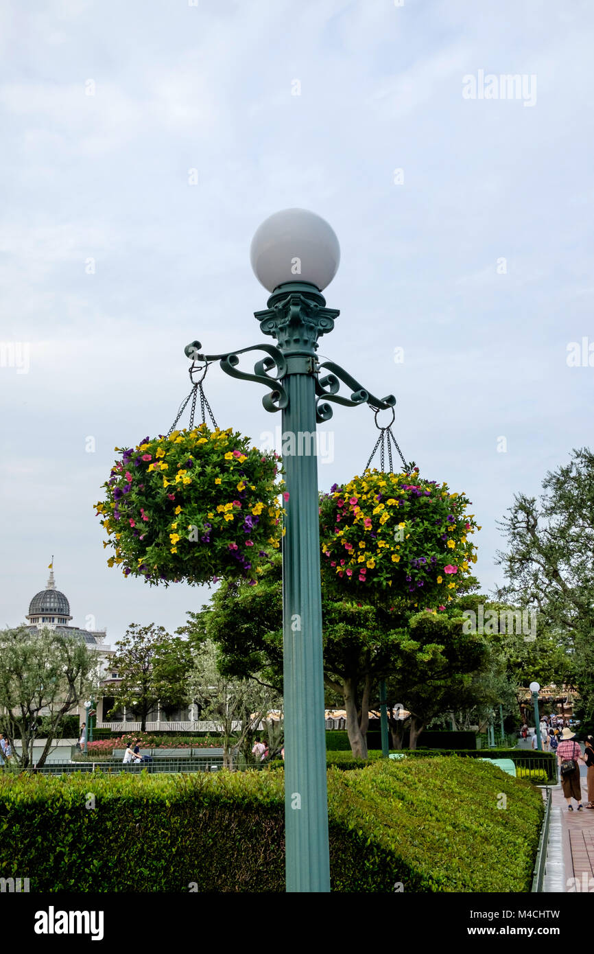 Ornate metal lamp post with round globe light on top with two baskets full of flowers hanging on either side. –Disneyland Tokyo Stock Photo