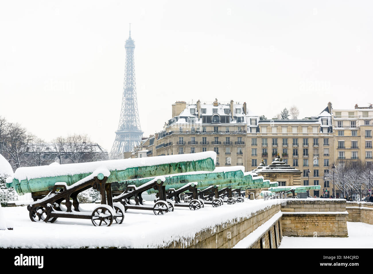 Winter in Paris in the snow. The row of bronze cannons of the Place des Invalides with a parisian building and the Eiffel tower in the background. Stock Photo