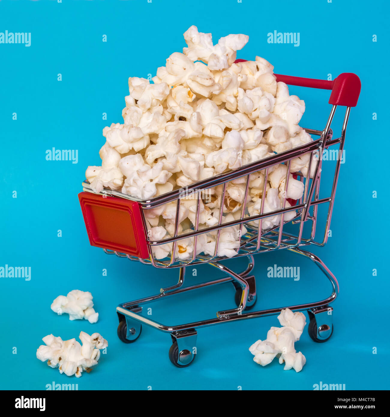Popcorn in a shopping trolley. A bunch of popcorn on a blue background. Surrealistic concept. Stock Photo