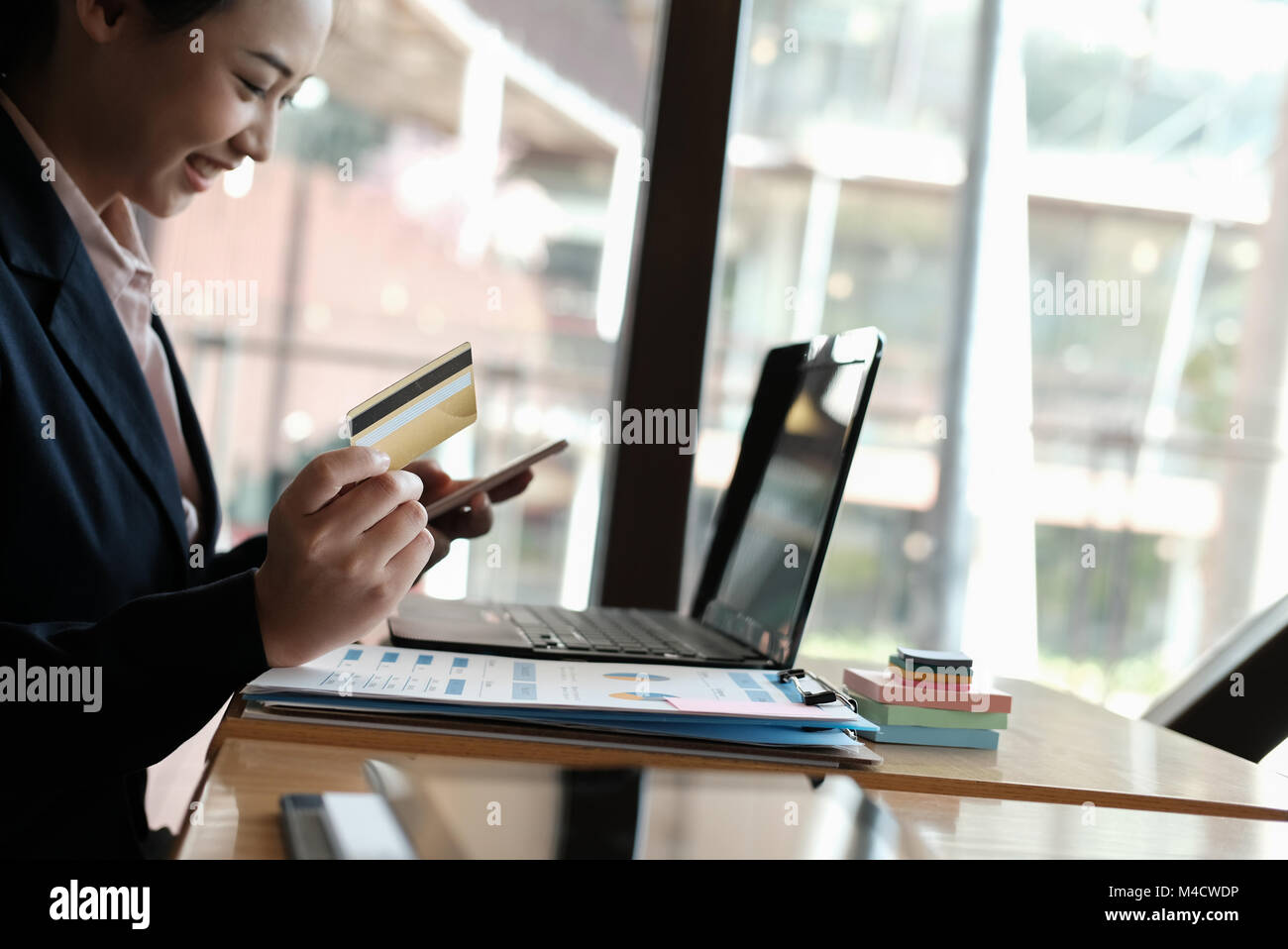 young woman holding a credit card and using smart phone for online shopping at cafe. businesswoman purchase goods from internet at office. female adul Stock Photo