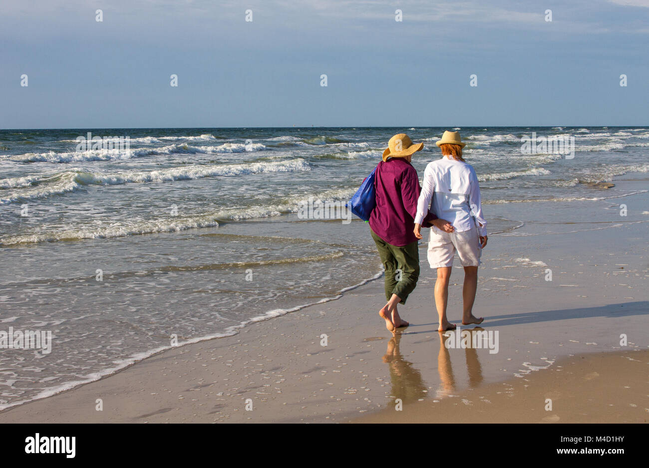 Two American senior citizen women walk together on a beach in the early morning. Stock Photo